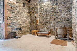 A stone-walled room with a wooden table, a sofa, and a large barrel. - 4 Bed in Bassenthwaite (oc-m40272) (Wythop)