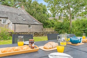An outdoor breakfast setup with croissants, juice, and a teapot on a table with chairs. - 4 Bed in Bassenthwaite (oc-m40272) (Wythop)
