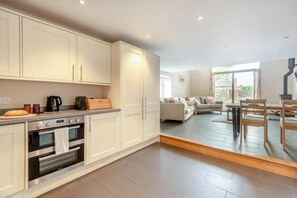 Eine moderne Küche mit eingebauten Geräten, ein Essbereich mit Tisch und Stühlen sowie ein Wohnzimmer mit Sofa und Kamin.