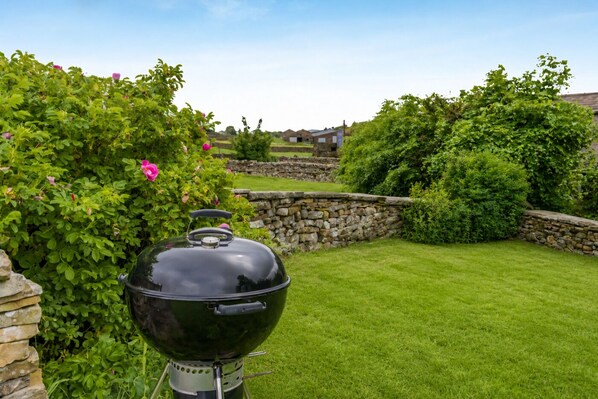 A backyard with a black barbecue grill, stone walls, and lush greenery.