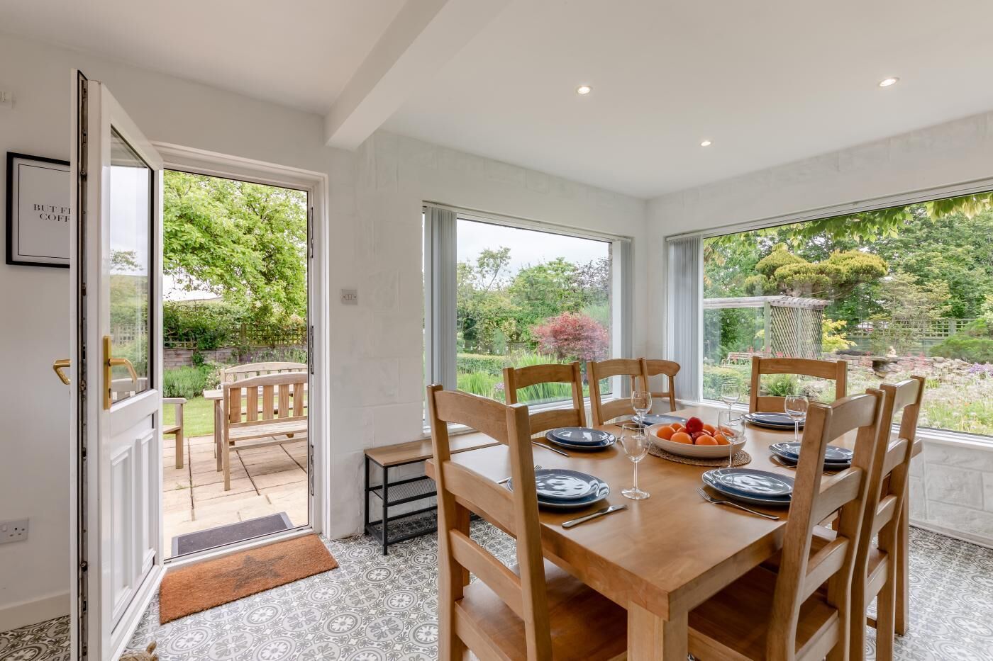 Ein Esszimmer mit Tisch für sechs Personen, großen Fenstern und Blick auf einen Garten.