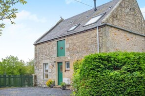 A stone building with a green door, windows, and a small garden area. - 3 Bed in Coldstream (oc-c39085) (Coldstream)