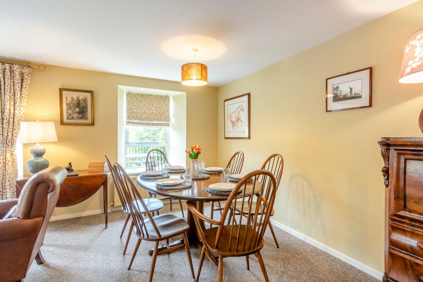 A dining room with a round table, wooden chairs, a chandelier, and framed pictures on the walls.
