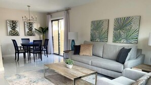Ein modernes Wohnzimmer mit einem grauen Sofa, einem Holztisch und einem Essbereich inklusive Tisch und Stühlen.