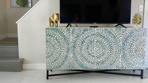 Ein Fernseher auf einem Schrank mit Mosaikmuster, eine Treppe und eine Pflanze an der Wand.