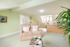 A cozy living room with a sofa, a coffee table with a magazine, and a kitchen area in the background. - 1 Bed in Raithby (oc-h42745) (Raithby)