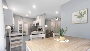 A modern kitchen with white cabinets, a dining area with a wooden table, and a ceiling fan. - Ranch Style Home_Easy Access to HWY_Sleeps 6 (Avondale)
