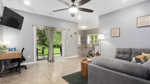 A modern living room with a grey sofa, a wooden coffee table, a ceiling fan, and a TV mounted on the wall. - Ranch Style Home_Easy Access to HWY_Sleeps 6 (Avondale)