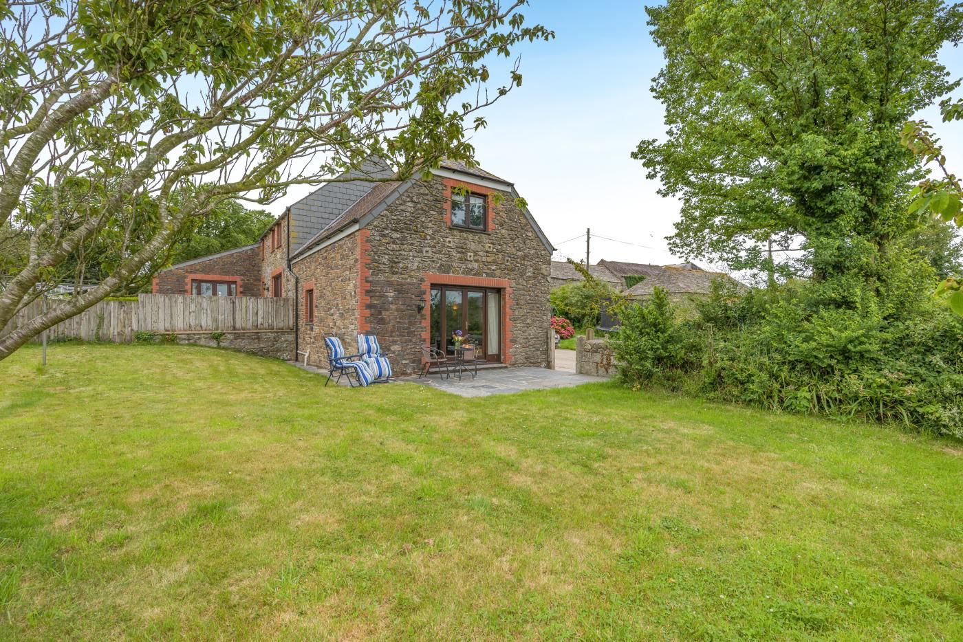 A stone house with a sloped roof, a fenced backyard, and a patio with chairs.
