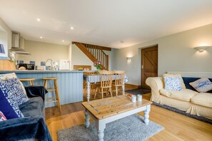 A cozy living room with a sofa, a coffee table, and a dining area with a table and chairs. - 1 Bed in St. Endellion (oc-p42706) (Trelights)