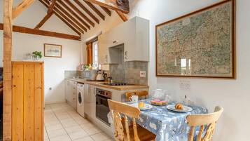 A kitchen with wooden beams, a dining table with a blue tablecloth, and a map on the wall.