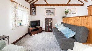 A living room with a television, sofa, and wooden beams on the ceiling.