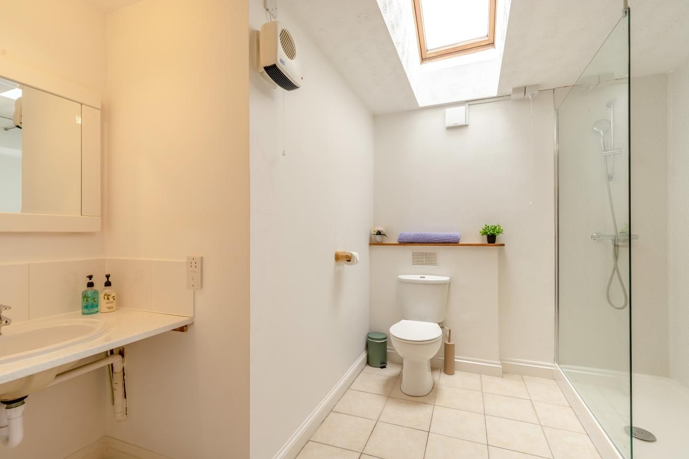 A bathroom with a skylight, a toilet, a shower, and a sink.
