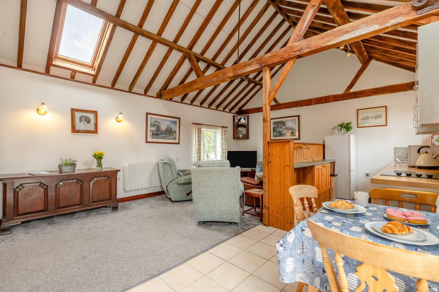 A cozy room with a wooden ceiling, a dining table with plates of food, a sofa, and a radiator.