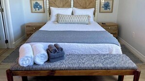 Una cama bien hecha con un edredón estampado, dos almohadas y toallas enrolladas sobre un banco de madera.