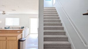 Un escalier avec des marches recouvertes de moquette et une rampe, menant à une pièce lumineuse dotée d’une fenêtre.