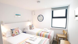 Habitación de hotel con dos camas, una ventana, una silla, un espejo y una lámpara en el techo.