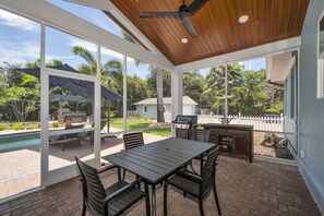 A covered patio with a table and chairs, a grill, and a pool in the background. - Ozona Oasis ~ Pool + Spa ~ Huge private lot near the Gulf (Palm Harbor)