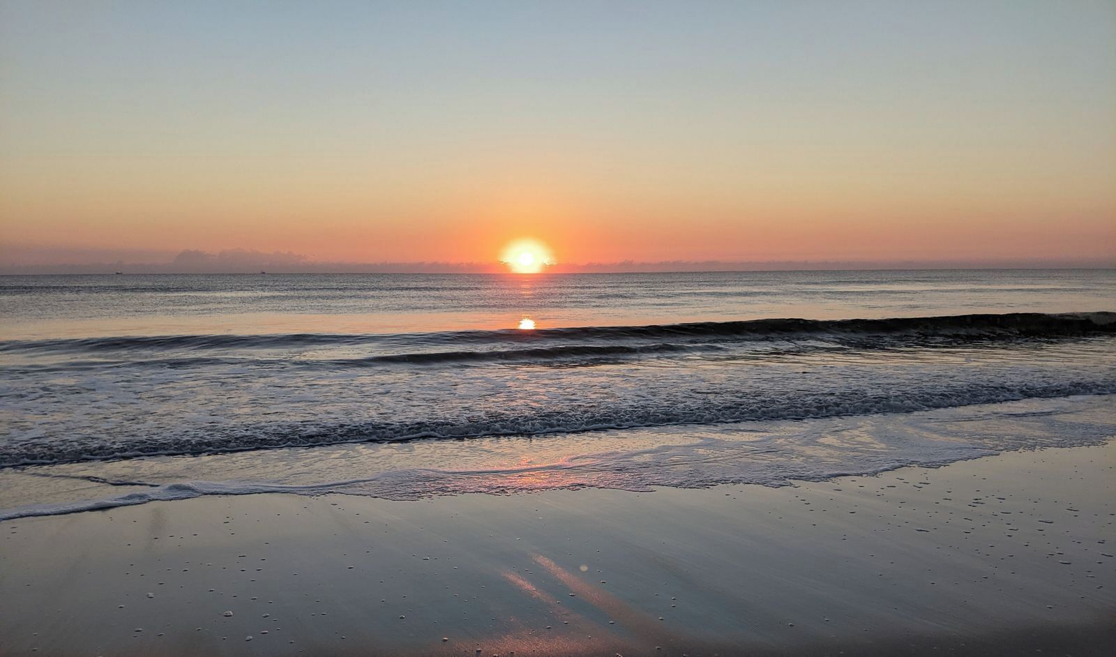 Uma praia com o sol se pondo sobre a água.
