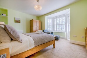 Ein Schlafzimmer mit Bett, Kleiderschrank, Sessel, Fenster mit Jalousien und einer Pendelleuchte.