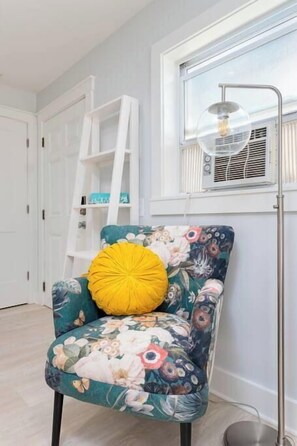 Ein Sessel mit floralem Bezug und einem gelben Kissen, eine weiße Leiter und ein Fenster mit Heizkörper.