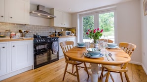 A kitchen with white cabinets, a stove, oven, and a dining table set with blue plates and a vase of flowers. - 2 Bed in Church Knowle (oc-c42784) (Creech)