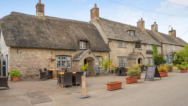 A traditional stone building with a thatched roof, outdoor seating, and potted plants. - 2 Bed in Church Knowle (oc-c42784) (Creech)