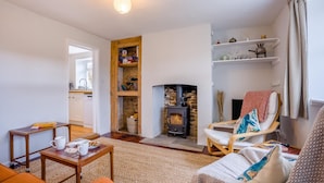 A cozy living room with a fireplace, a wooden shelf with books, a comfortable chair, and a coffee table. - 2 Bed in Church Knowle (oc-c42784) (Creech)
