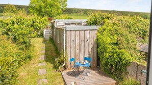A wooden shed with a table and chairs outside, surrounded by greenery and a stone path. - 2 Bed in Church Knowle (oc-c42784) (Creech)