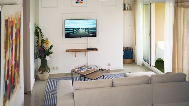 Una sala de estar moderna con un televisor de pantalla plana grande, un sofá, una mesa de centro, un ventilador de techo y vistas a través de un patio corredero de vidrio.