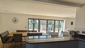 Una cucina moderna con un'isola centrale, una zona pranzo con una panca e ampie porte scorrevoli in vetro che danno su uno spazio esterno.
