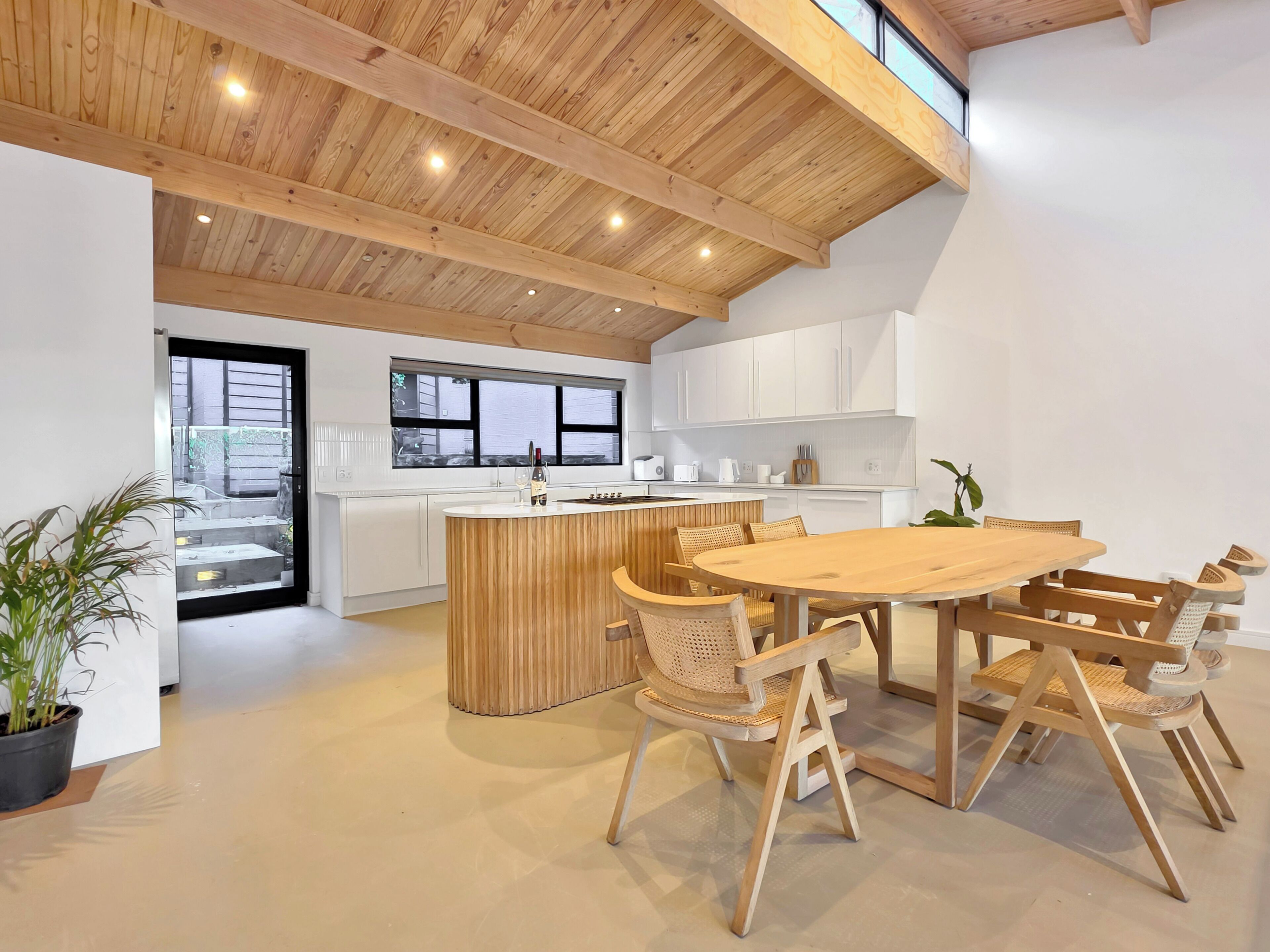 Une cuisine moderne avec des poutres en bois au plafond, un îlot central et un coin repas avec des chaises en bois.