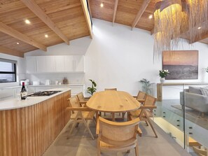 Eine moderne Küche mit weißen Schränken, einer Holzinsel mit eingebautem Herd und einem Essbereich mit einem runden Holztisch und Korbstühlen.