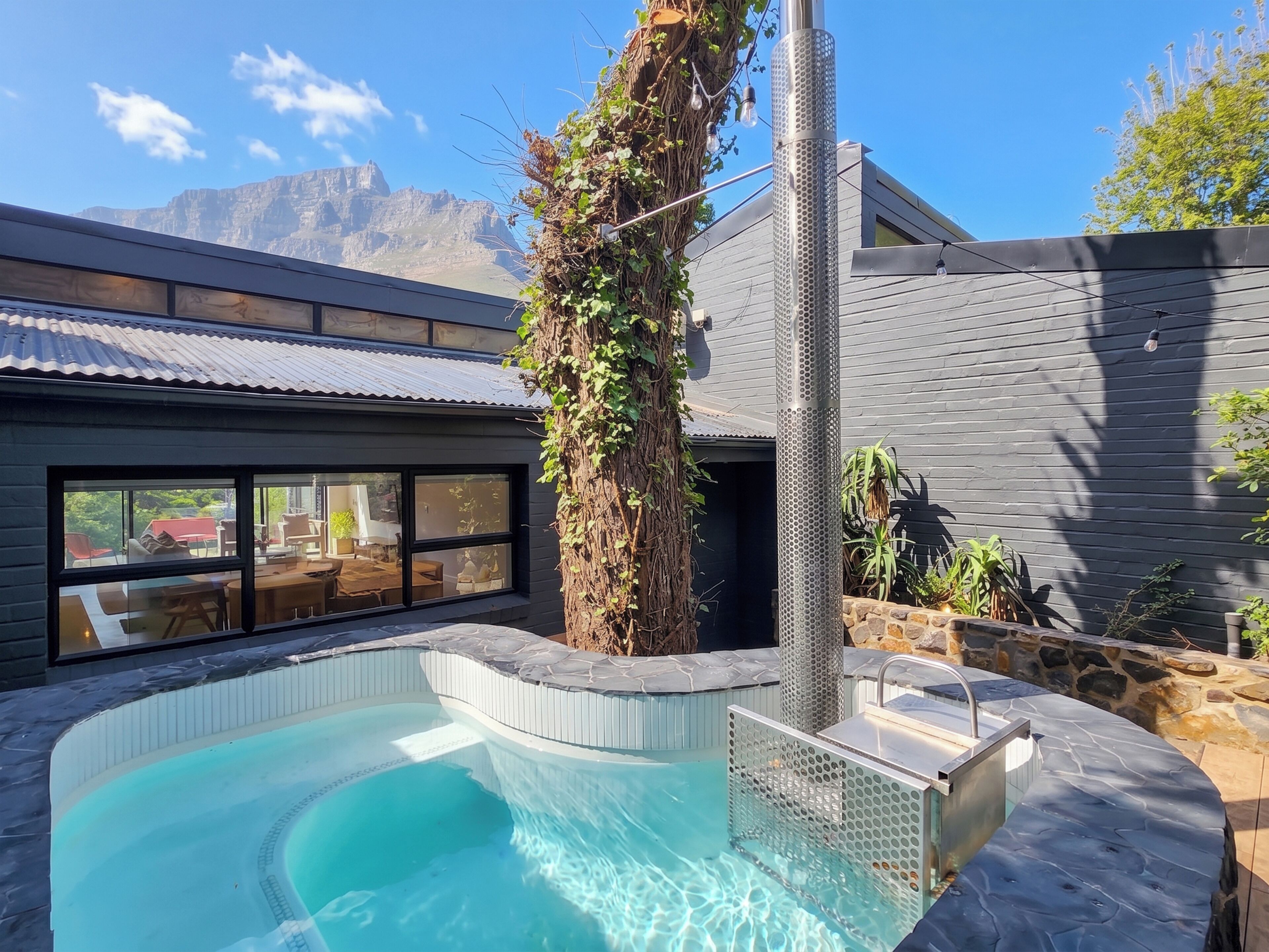 A swimming pool with a stone edge, a pergola with climbing plants, and a view of mountains in the background.