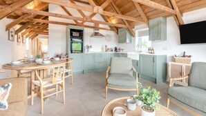 Eine geräumige Küche mit hohen Decken und freiliegenden Balken, ein Essbereich mit Holzmöbeln und eine gemütliche Sitzecke mit Sofa und Sesseln.