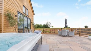 Ein Whirlpool neben einem Holzgebäude mit einer Terrasse, die Korbmöbel und einen Gartenblick bietet.