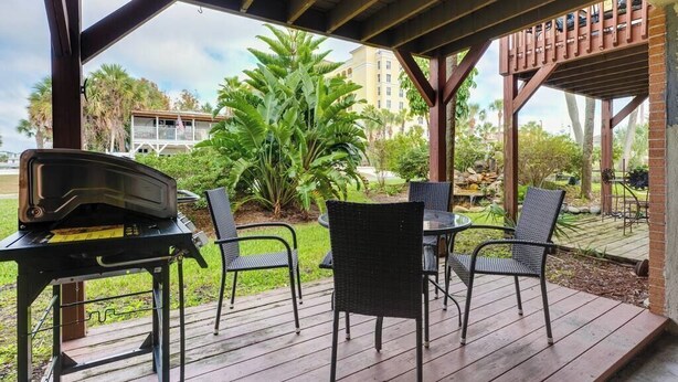 Patio esterno con barbecue, sedie e vista su un edificio e palme.