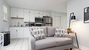 Una cucina moderna con mobili bianchi, un divano grigio con cuscini decorati e un lampadario nero.