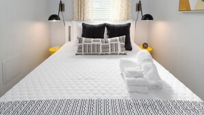 Un letto rifatto con cura, un copriletto bianco, due cuscini neri e un set di asciugamani bianchi.