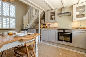 Une cuisine avec une table en bois, des chaises, un escalier et un four encastré.