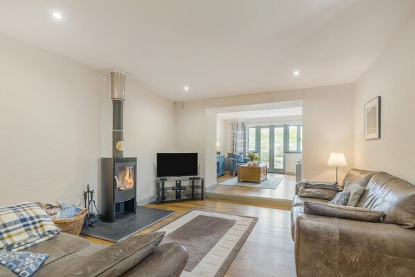 A living room with a fireplace, leather sofas, a TV, and a large window. - 2 Bed in Dwrbach (oc-e42726) (Dwrbach)