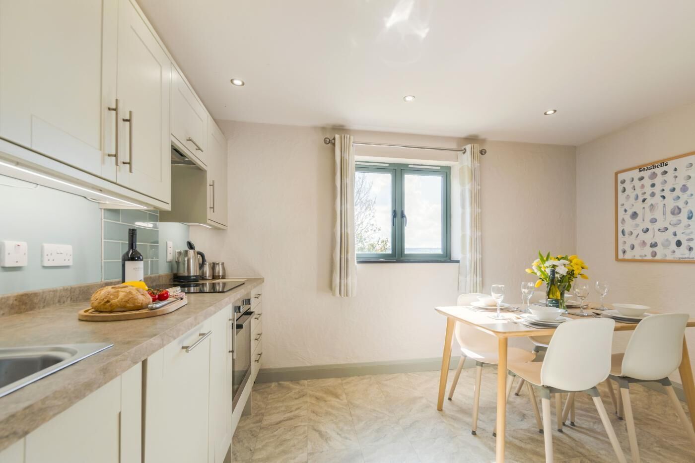 Une cuisine moderne avec des meubles blancs, un coin repas comprenant une table et des chaises, et une fenêtre avec des rideaux.