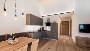 A modern kitchen with wooden cabinets, a dining table with chairs, and a TV mounted on the wall. - Cozy vacation rental with a spacious loggia and a magnificent view (Trentino-Alto Adige)