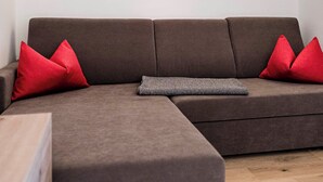 A modern living room with a sectional sofa, red cushions, a wall-mounted light, and a framed picture. - Cozy vacation rental with a spacious loggia and a magnificent view (Trentino-Alto Adige)