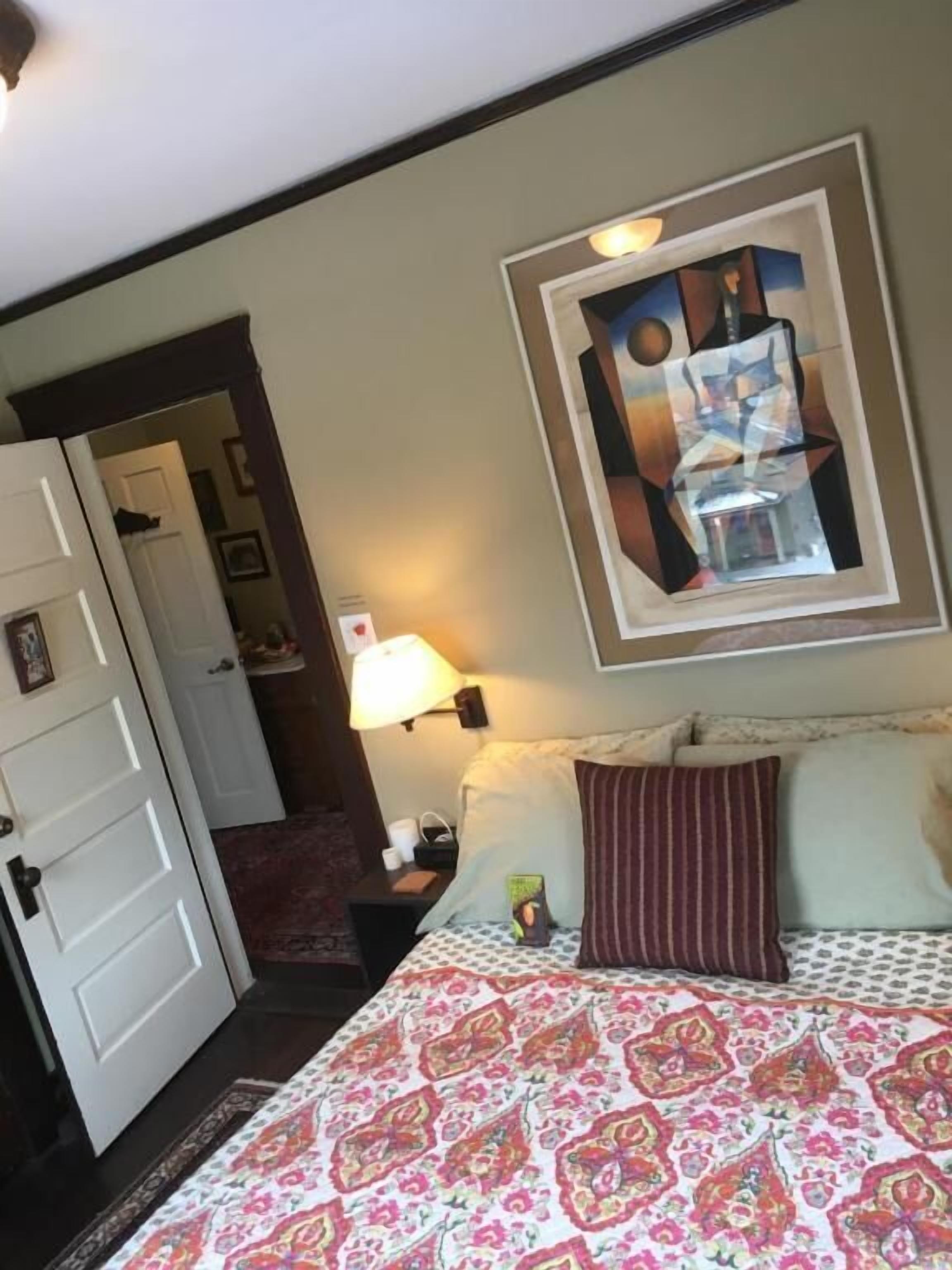 Une chambre d’hôtel avec un lit, une table de chevet, une lampe, un tableau et une porte.