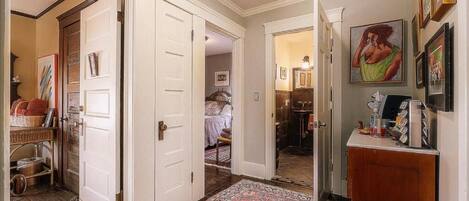 A hallway with a patterned rug, a red stool, and a door leading to a bedroom.