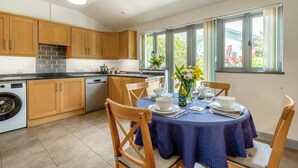 A modern kitchen with wooden cabinets, a built-in dishwasher, and a dining area with a blue tablecloth and chairs. - 2 Bed in Dwrbach (oc-w42727) (Dwrbach)