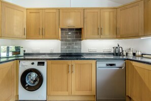 A kitchen with wooden cabinets, a washing machine, a dishwasher, and a tiled backsplash. - 2 Bed in Dwrbach (oc-w42727) (Dwrbach)