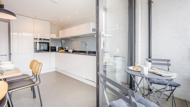 A modern kitchen with white cabinets, a dining area with a table and chairs, and a balcony with a table and chairs. - 2 Bed in Swanage (oc-c41747) (Swanage)