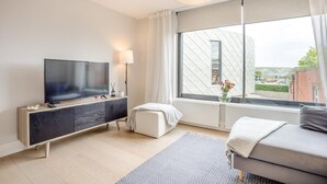 A modern hotel room with a flat-screen TV, a sofa, a small table, and a large window offering a view of the city. - 2 Bed in Swanage (oc-c41747) (Swanage)
